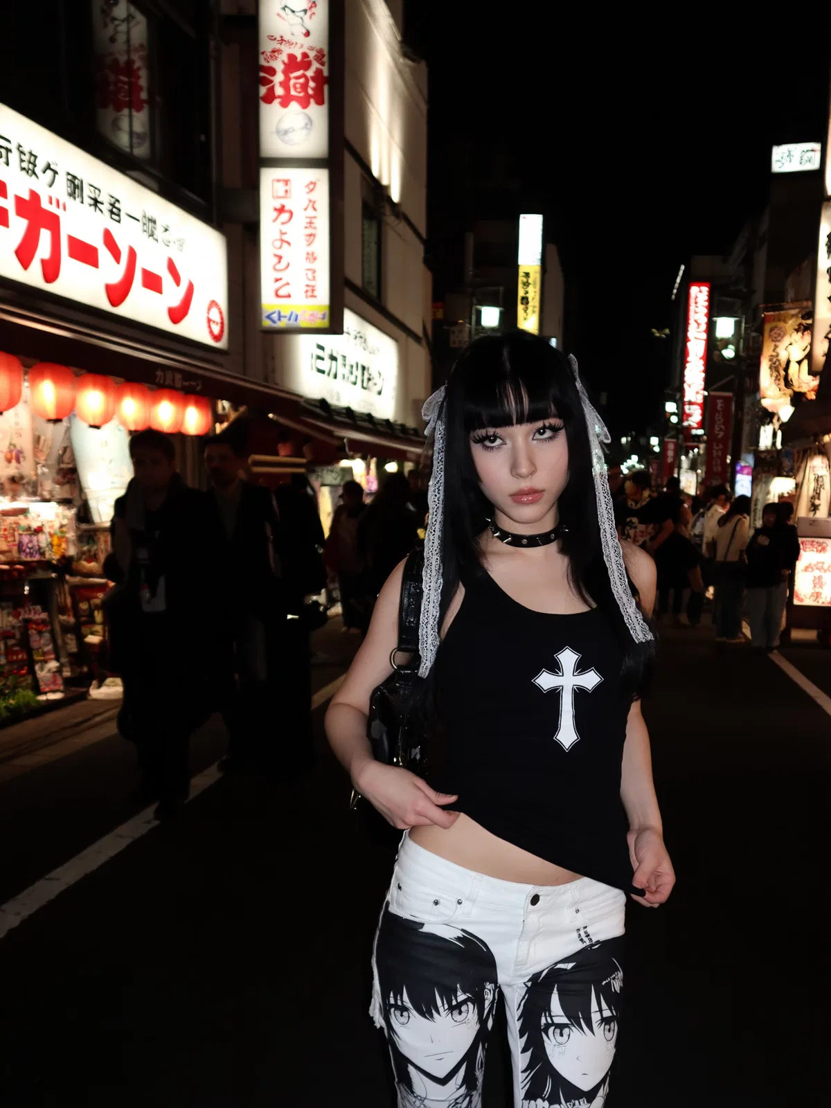Goth girl standing on a busy neon-lit street at night in a black cross top and white anime-print shorts